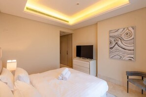 A hotel room with a bed, a flat-screen TV, a painting, and a chair. - Beachfront Luxury Apt w/ Sea Views & Infinity Pool (Dubai)