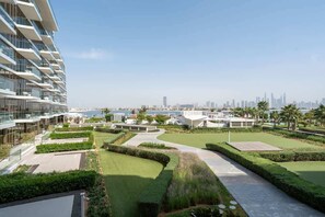 A modern building with a rooftop garden, a view of the city skyline, and a body of water in the background. - Beachfront Luxury Apt w/ Sea Views & Infinity Pool (Dubai)