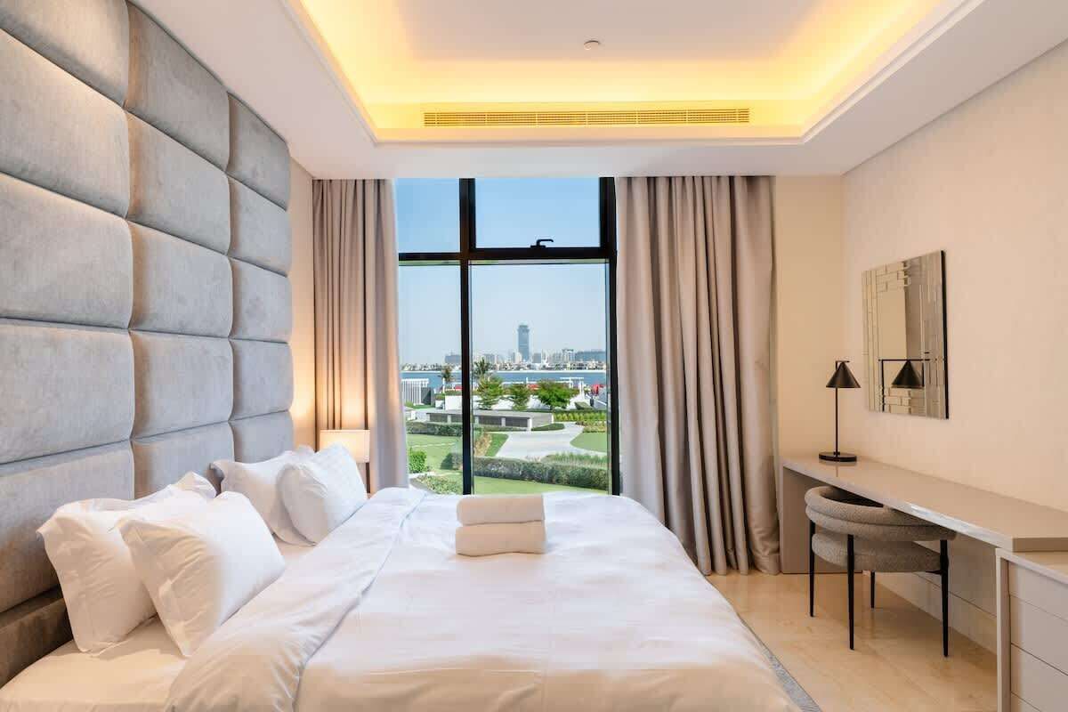 A modern hotel room with a large bed, a desk, and a view of the cityscape.