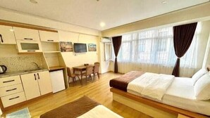 A compact hotel room with a bed, a small kitchenette, a dining area, and a large window with curtains. - N-V Suites (Istanbul)