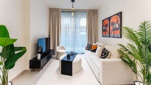 Un salon moderne avec un canapé, une table basse, un téléviseur et une grande fenêtre avec des rideaux.
