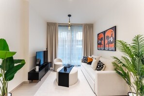 Un salon moderne avec un canapé, une table basse, un téléviseur et une grande fenêtre avec des rideaux.