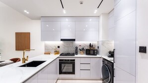 Une cuisine moderne avec des meubles blancs, un four encastré, un four à micro-ondes et un lave-linge.