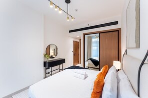 A modern hotel room with a large bed, a bedside table, a mirror, and a view of the outside.