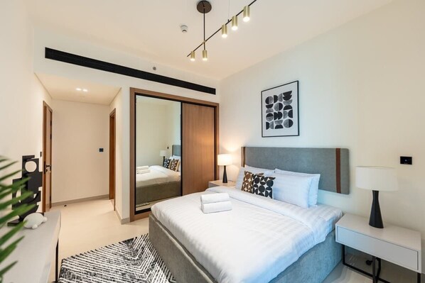 A modern hotel room with a large bed, bedside tables, a mirror, and a ceiling light fixture.