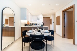 Un comedor moderno con una mesa redonda preparada para cuatro comensales, una cocina al fondo y un espejo grande a la izquierda.