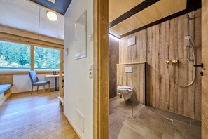 Et moderne badeværelse med et brusekabine i træ, toilet og bænk, i et rum med trægulv og et stort vindue.