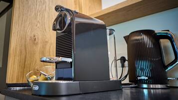 Una cafetera sobre una encimera de cocina con un estante de madera y una taza negra.
