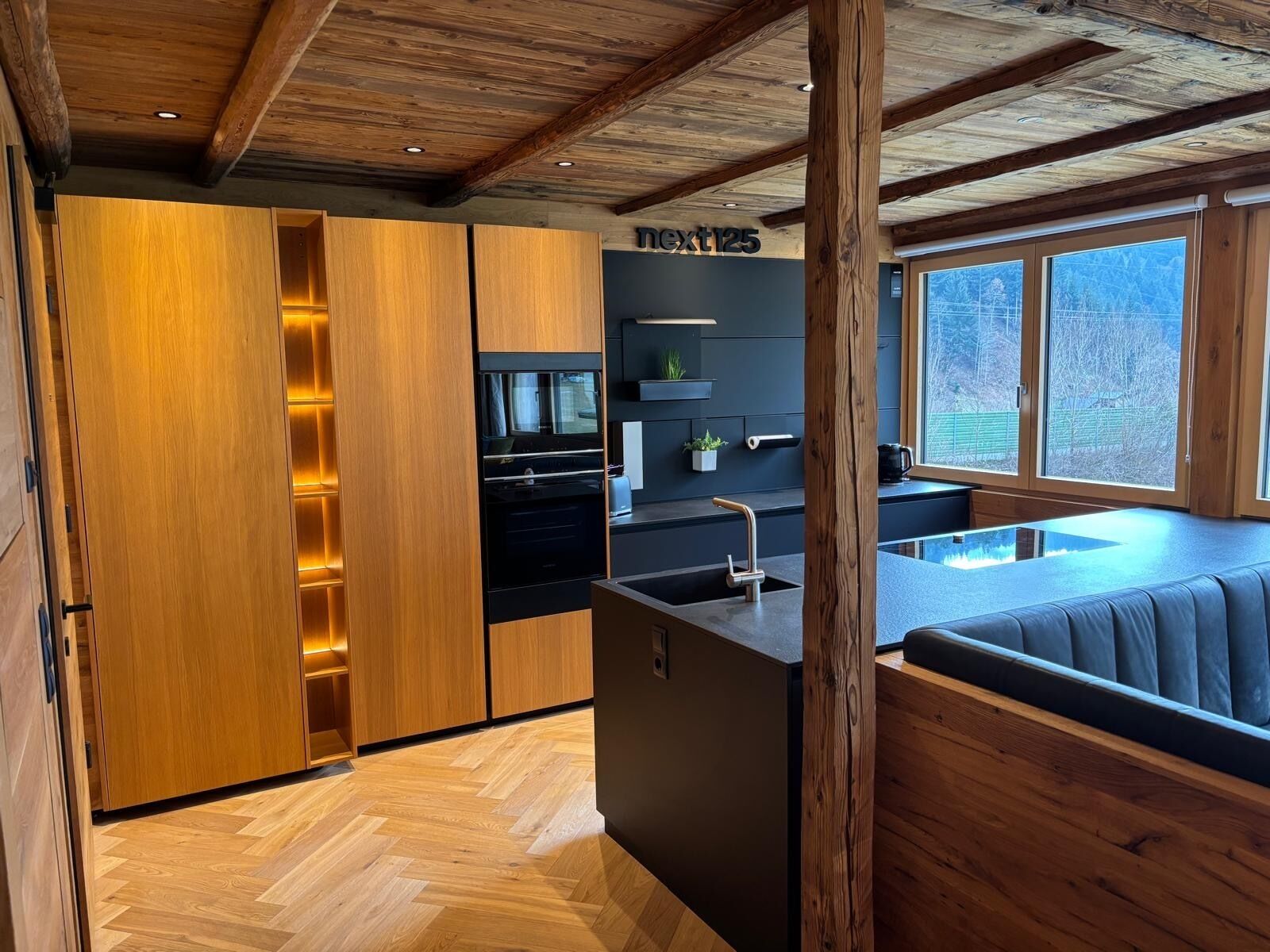 Une cuisine moderne avec des meubles de rangement en bois, un four encastré et un plan de travail noir.