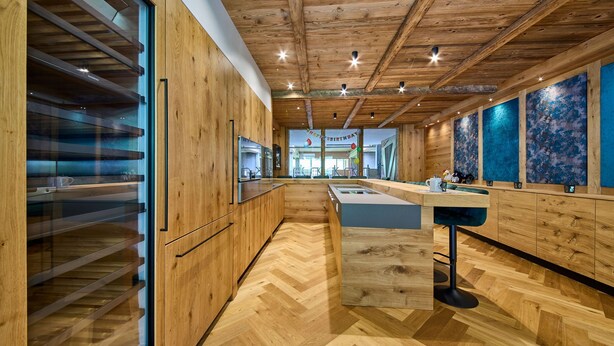 A modern kitchen with wooden cabinetry, a central island, and a herringbone floor pattern. - Bocks Apartments 53C (Dalaas)