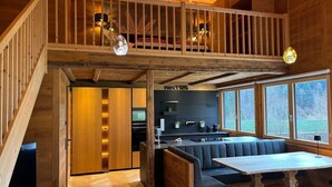 A modern loft-style interior with a wooden staircase, a dining area with a wooden table, and a kitchen with a black backsplash. - Bocks Apartments 53C (Dalaas)