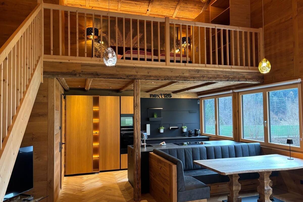 Un intérieur moderne de style « loft », avec un escalier en bois, un coin repas doté d’une table en bois et une cuisine avec un plan de travail noir.