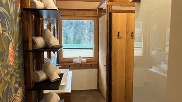 A bathroom with wooden shelves holding towels, a window with a view of trees, and a wooden door.