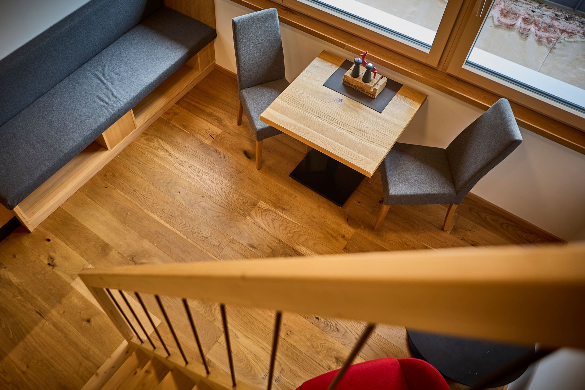 Un intérieur moderne avec un plancher en bois, un banc, deux chaises et une table agrémentée de salières et de poivrières.