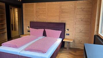 A bedroom with a wooden panel wall, a purple upholstered bed, checkered bedding, two bedside tables, and a herringbone-patterned floor.