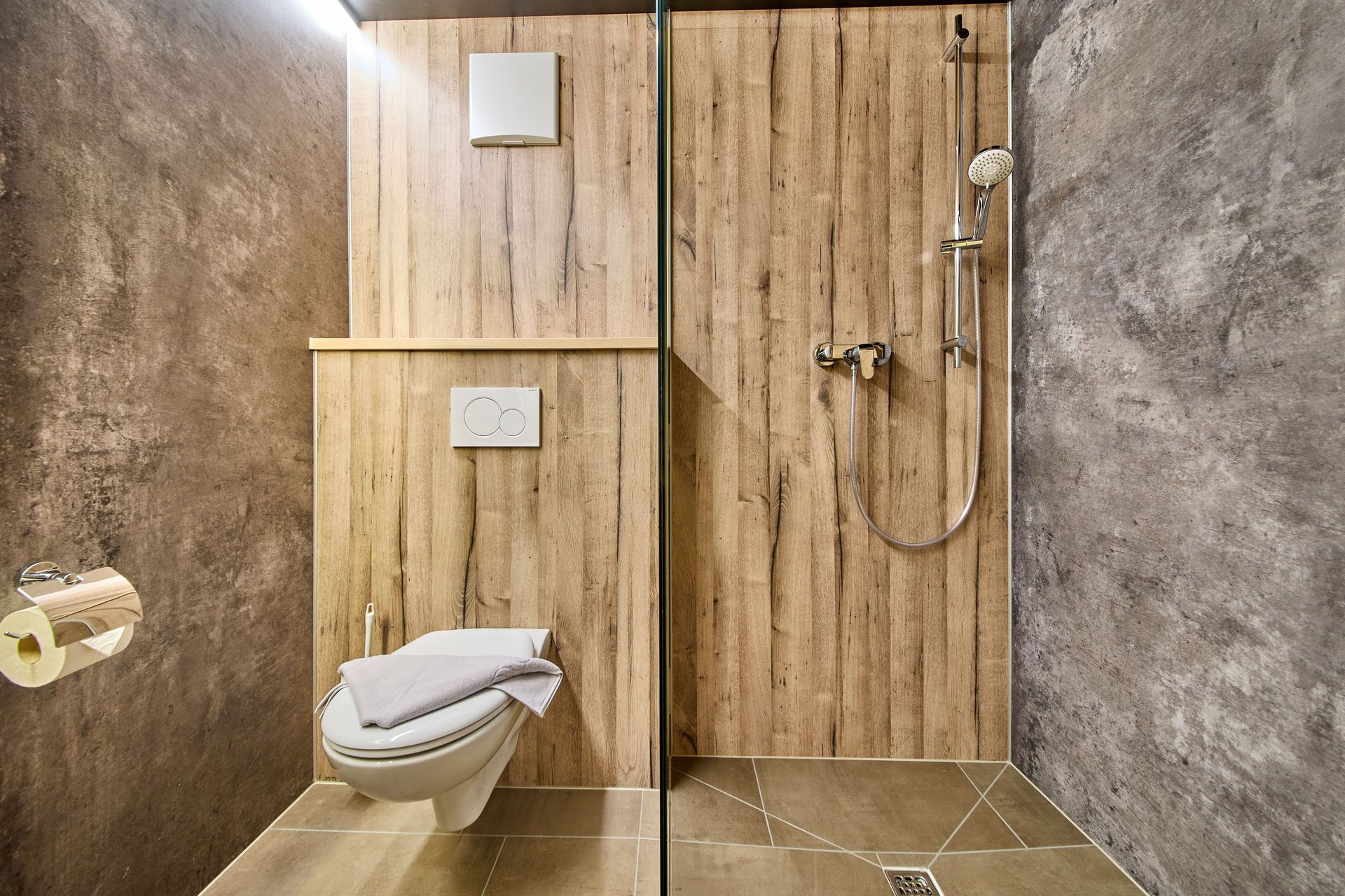 Un bagno con un mobile bagno in legno, un water, una doccia con soffione a mano e un porta asciugamani.