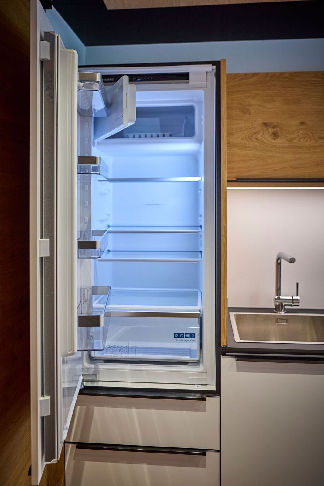 Un refrigerador abierto con varios estantes, un dispensador de agua incorporado y un lavamanos de acero inoxidable.