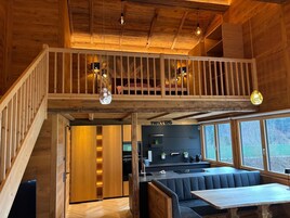 Un interior moderno estilo loft con una escalera de madera, un entresuelo con cama, una zona de cocina y un comedor con banco.