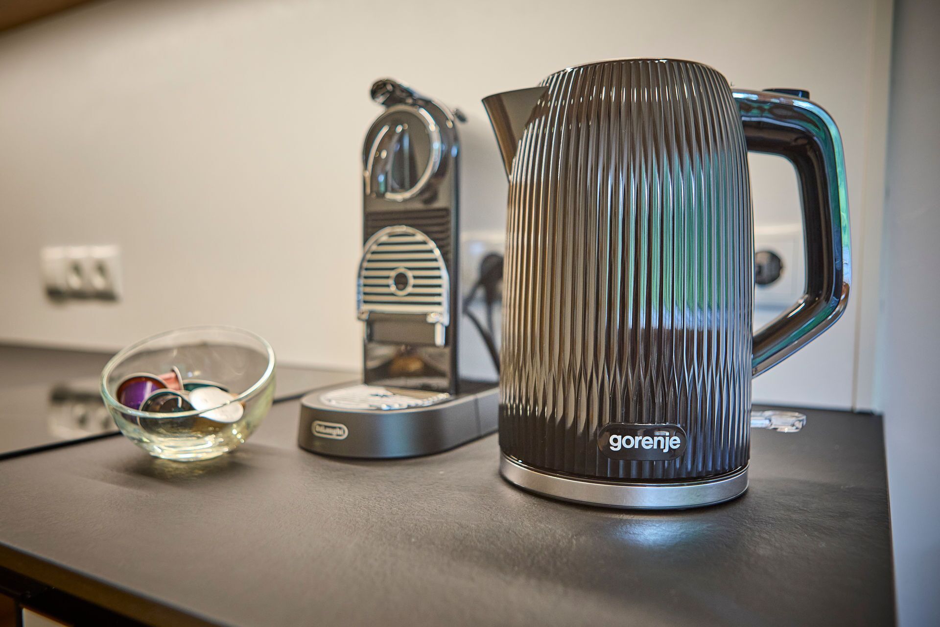 Una encimera de cocina con una cafetera, un hervidor y un bol de vidrio.