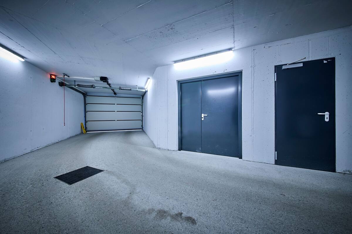 Un parking avec un sol en béton, un escalier en métal et deux portes.