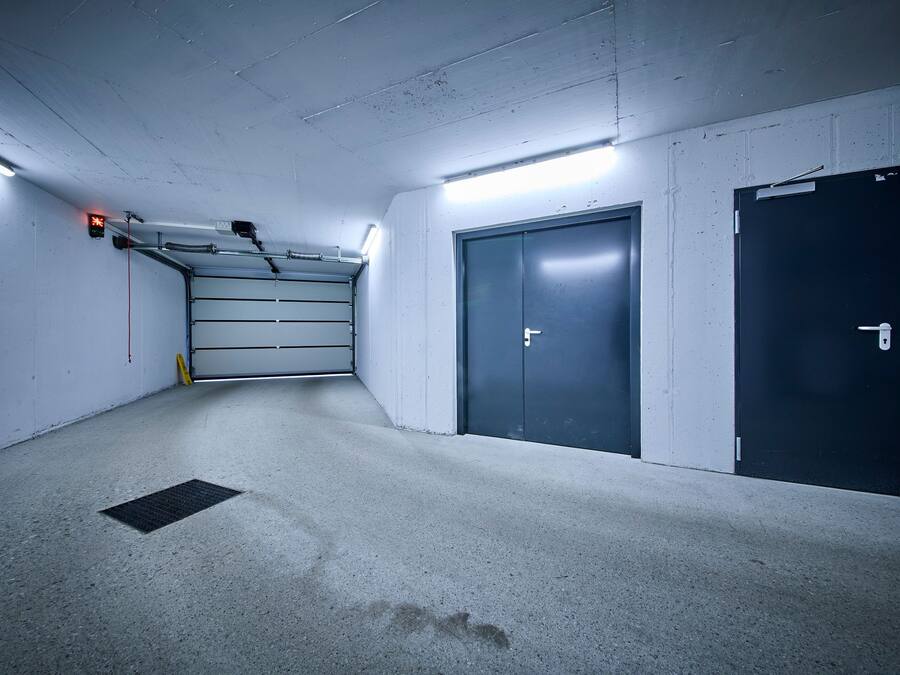 A parking garage with a concrete floor, a metal staircase, and two doors.