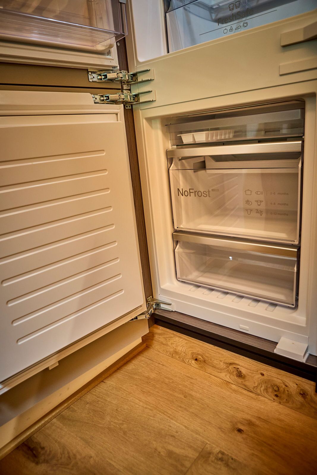 Een open koelkast met een 'NoFrost'-functie en een houten vloer.