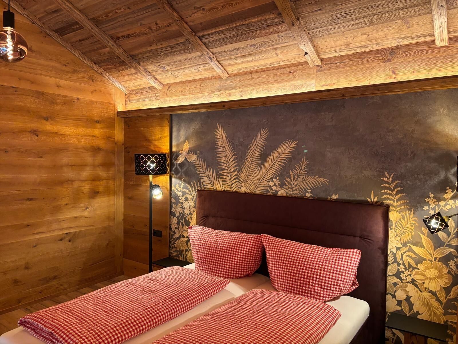 A wooden room with a bed, a nightstand, and a wall with a floral mural.