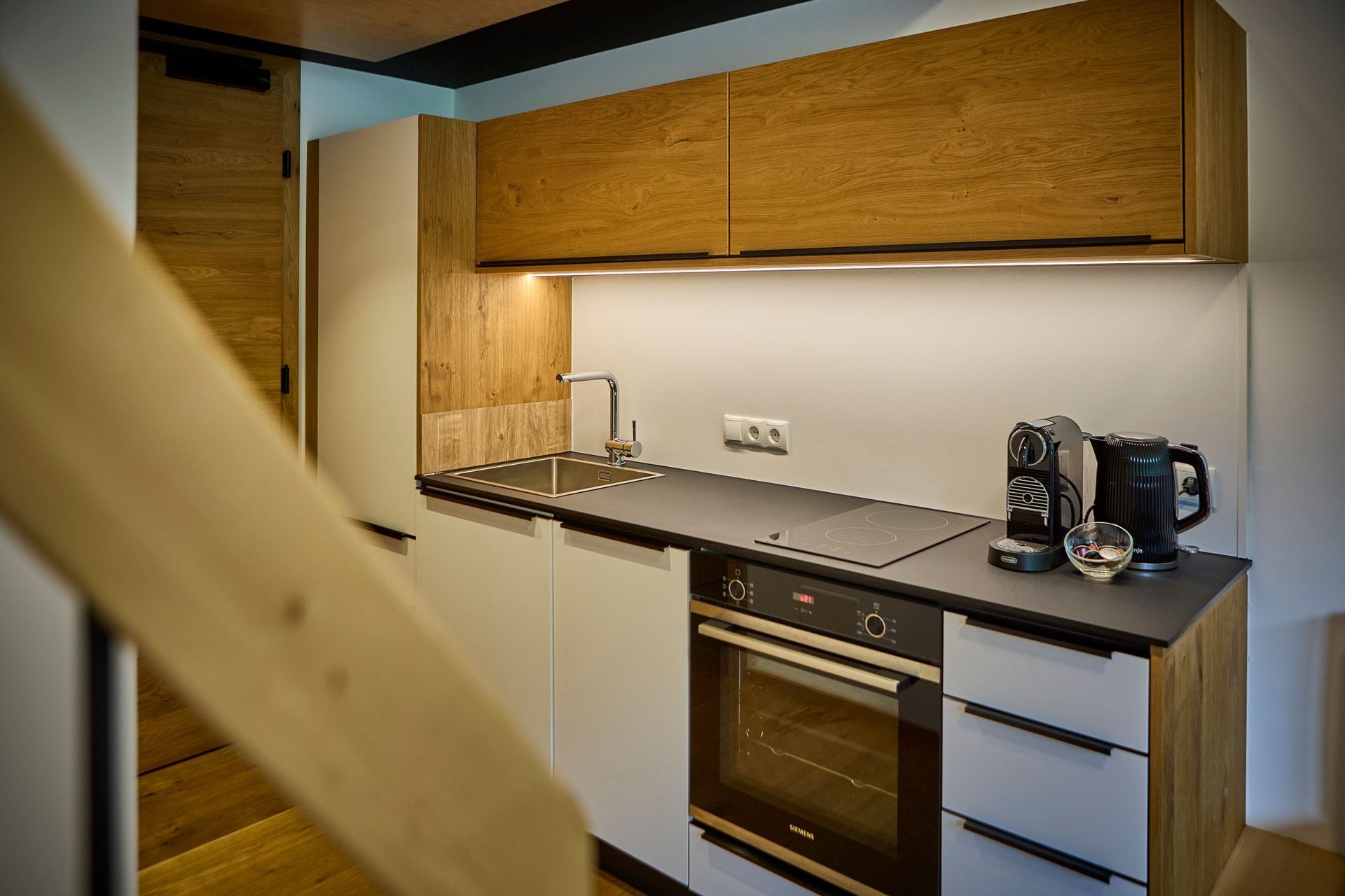 Une cuisine compacte avec des meubles en bois, un four encastré, une machine à café et un évier.