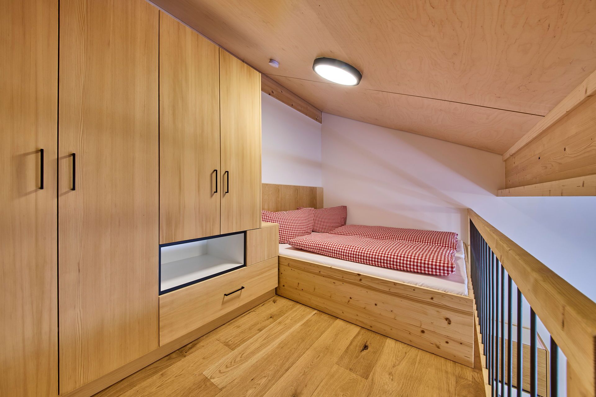 Ein gemütliches Schlafzimmer mit Holzschrank, Einzelbett mit karierter Bettwäsche und schrägem Dach mit Dachfenster.