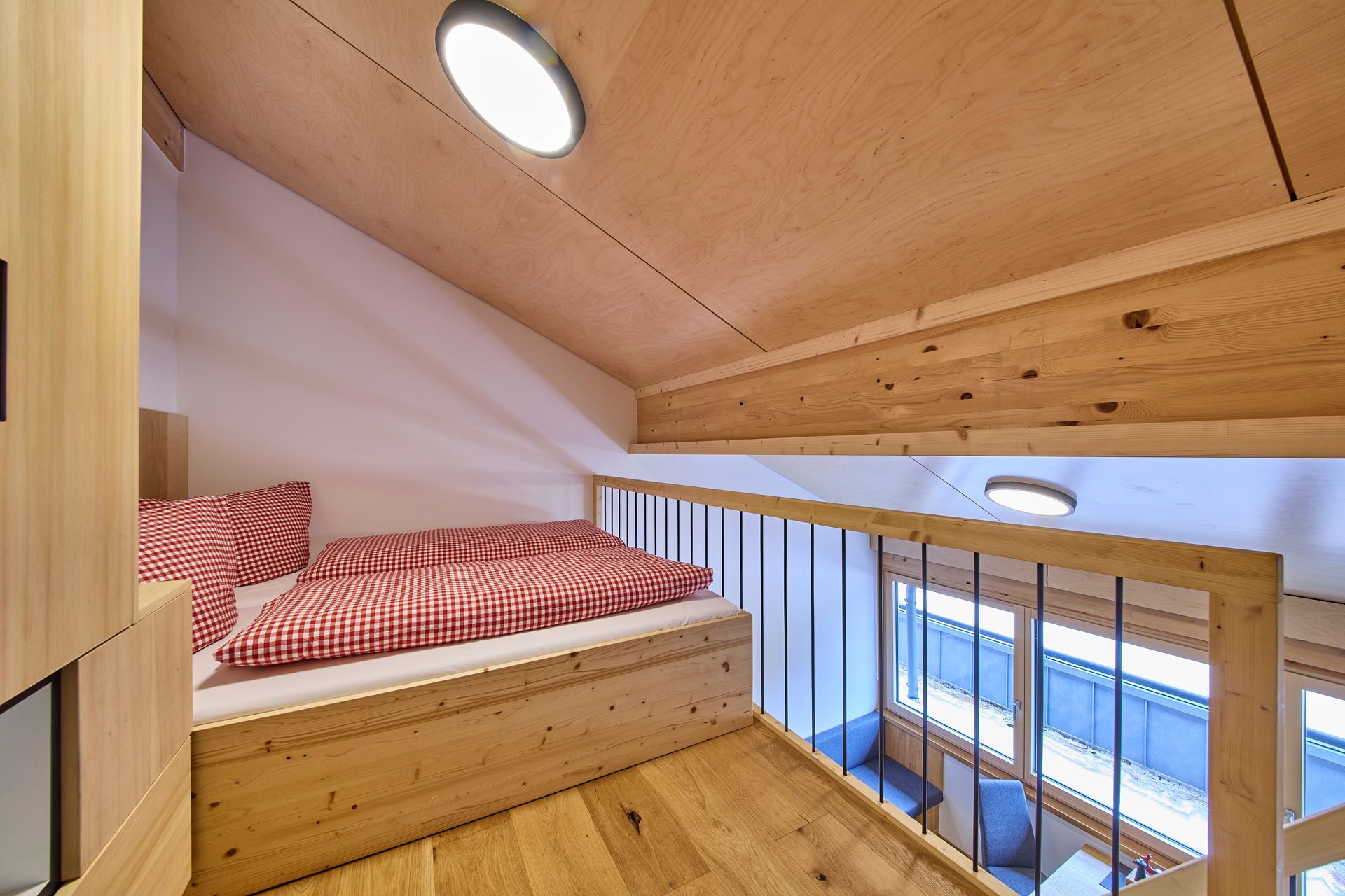 A wooden loft bedroom with a bunk bed, a small desk, and a window overlooking a snowy landscape.