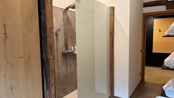 A modern bathroom with a glass shower enclosure, wooden accents, and a neatly made bed with towels.