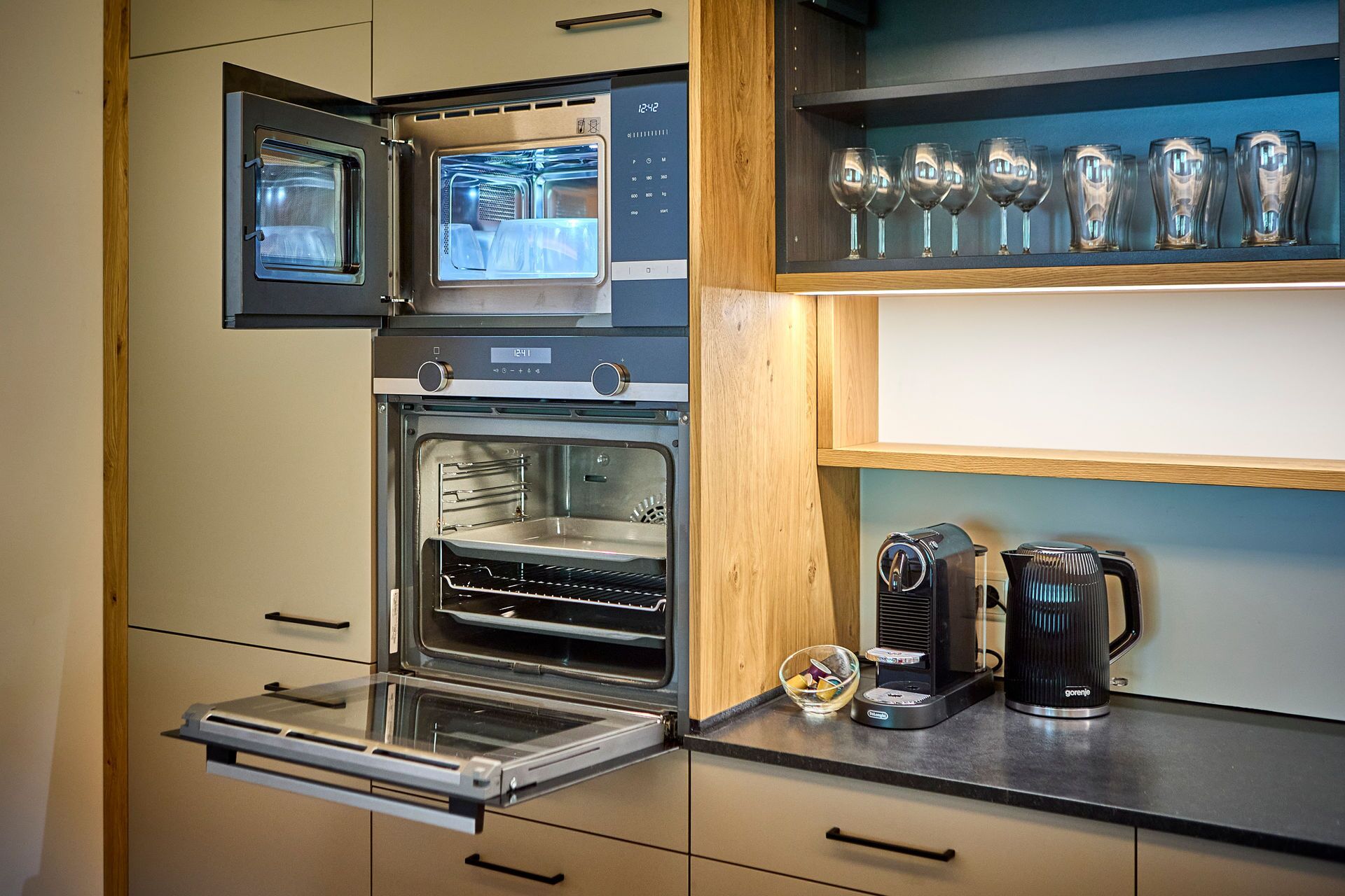 A compact kitchen with a built-in oven, a coffee maker, and a glassware holder.
