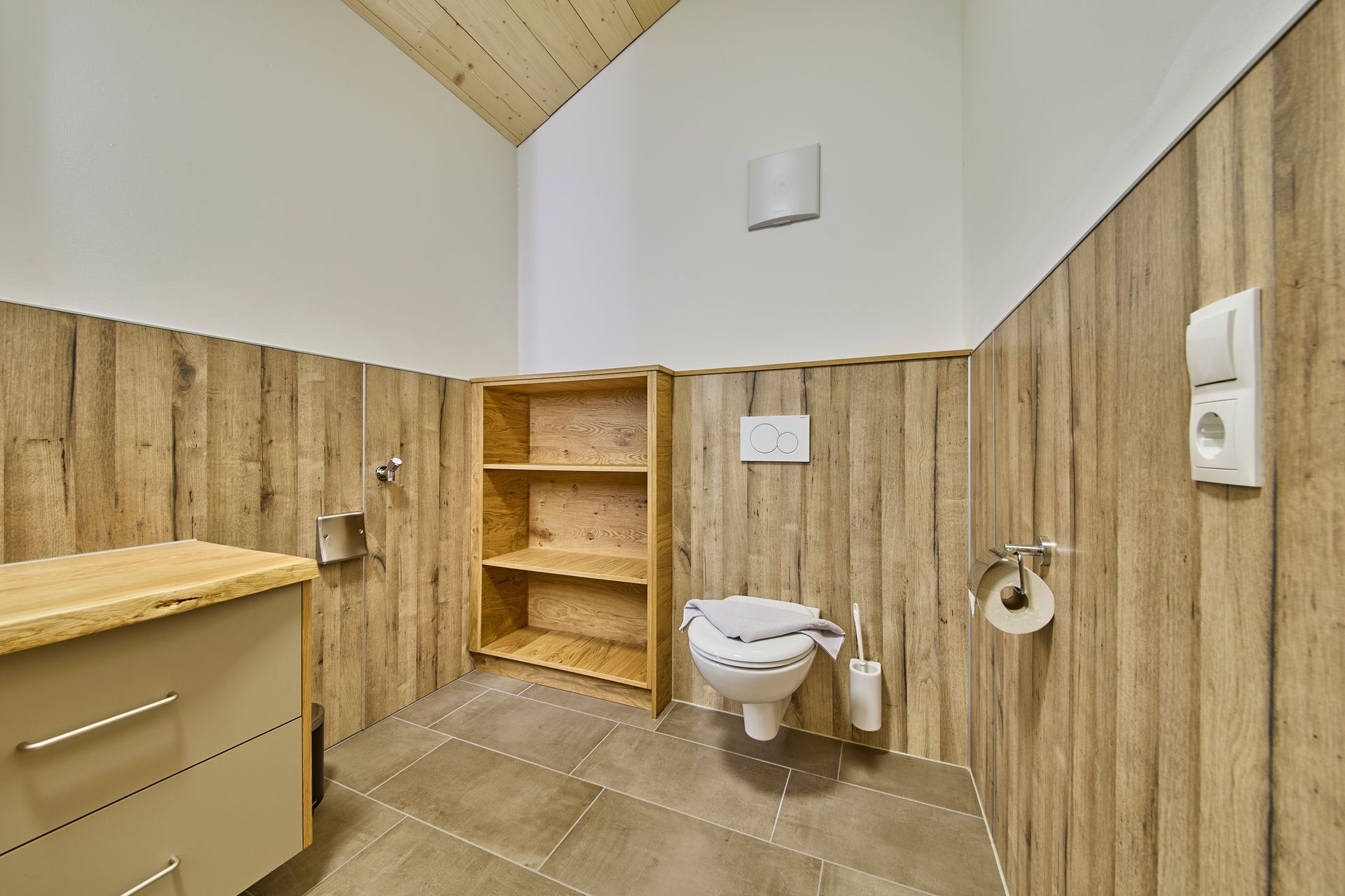 A compact bathroom with wooden paneling, a toilet, a sink, and a towel rack.