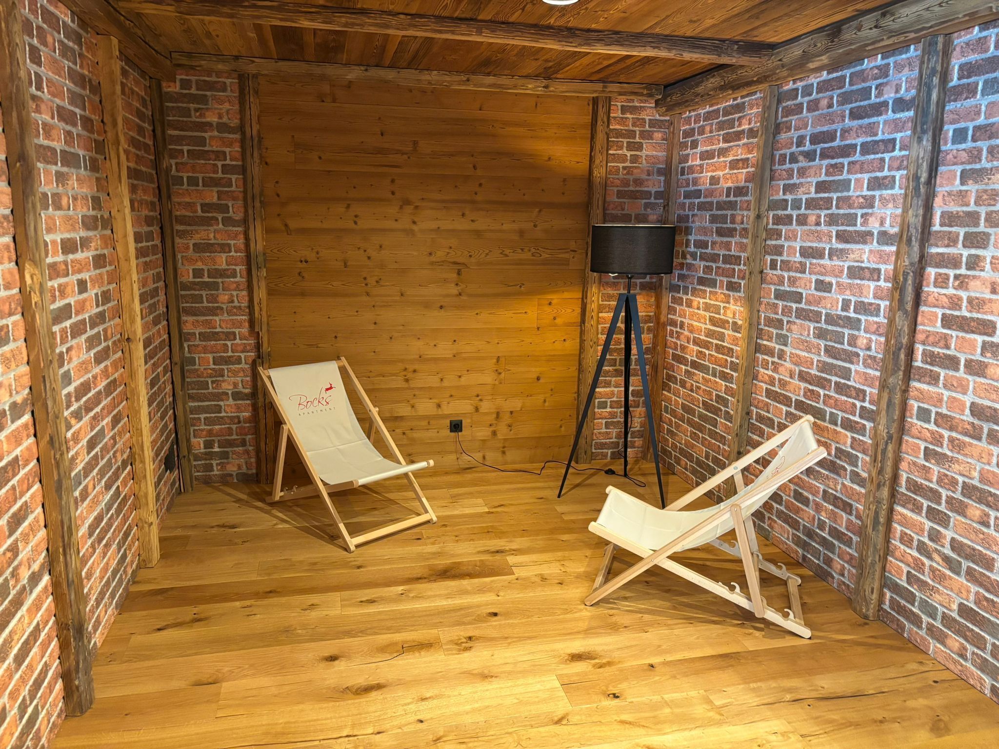 Una habitación con pisos de madera, paredes de ladrillo y dos sillas plegables blancas.