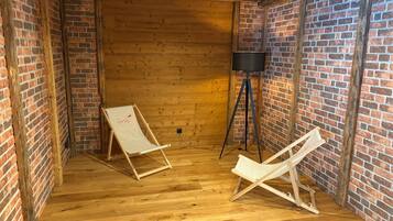 Una habitación con pisos de madera, paredes de ladrillo y dos sillas plegables blancas.