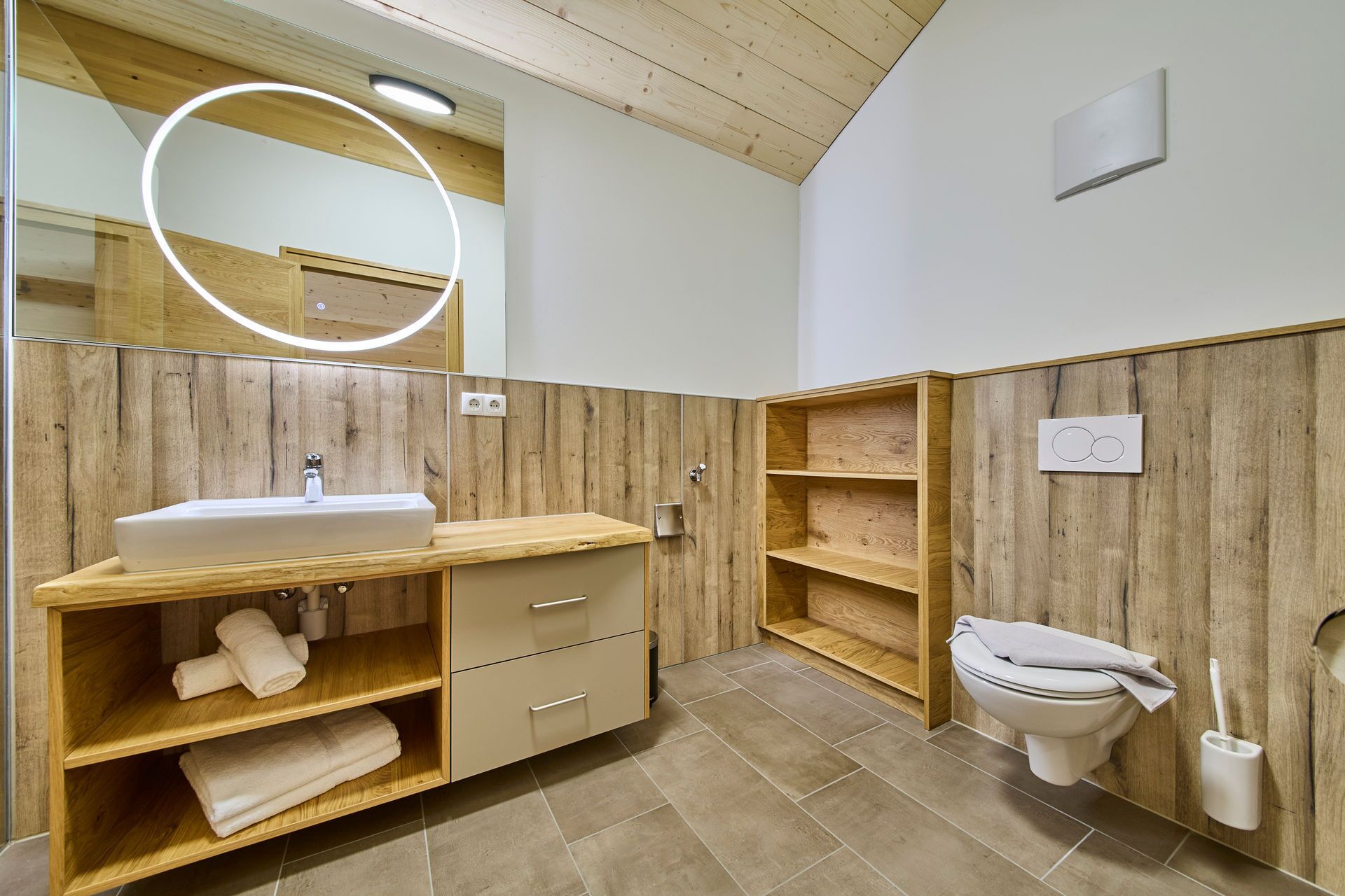 Un baño moderno con tocador de madera, inodoro y espejo con luz.