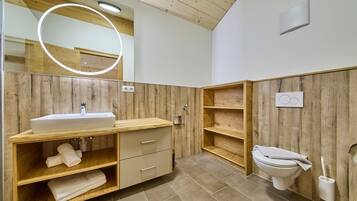 Un baño moderno con tocador de madera, inodoro y espejo con luz.