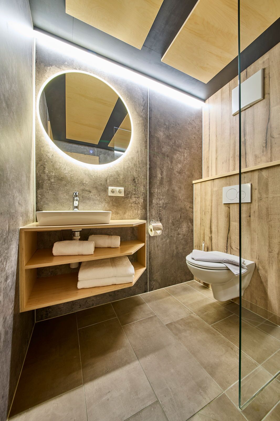 A modern bathroom with a wooden vanity, a round mirror, and a toilet.