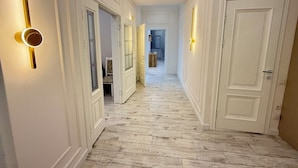 Un couloir aux murs blancs, au plancher en bois et aux portes dotées de luminaires.