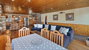 Amplia sala de estar con techo de madera, un conjunto de sofás, una mesa de comedor y una cocina al fondo.