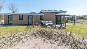 Ein modernes Haus mit einer großen Terrasse, einer überdachten Sitzgelegenheit und einem gepflegten Rasen.
