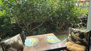 Eine Terrasse mit Tisch und zwei Stühlen, umgeben von Grünpflanzen und einer Steinmauer.