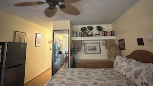 Ein Schlafzimmer mit Bett, Deckenventilator, Kühlschrank, Bücherregal und einer Tür zu einem anderen Raum.