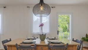 Un comedor con una mesa de madera dispuesta para dos personas, una orquídea en maceta y una lámpara colgante.