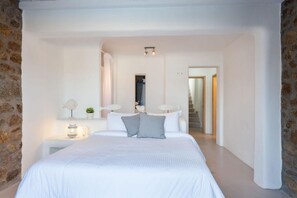 A spacious bedroom with a large bed, bedside lamps, and a view of a staircase leading to another room.