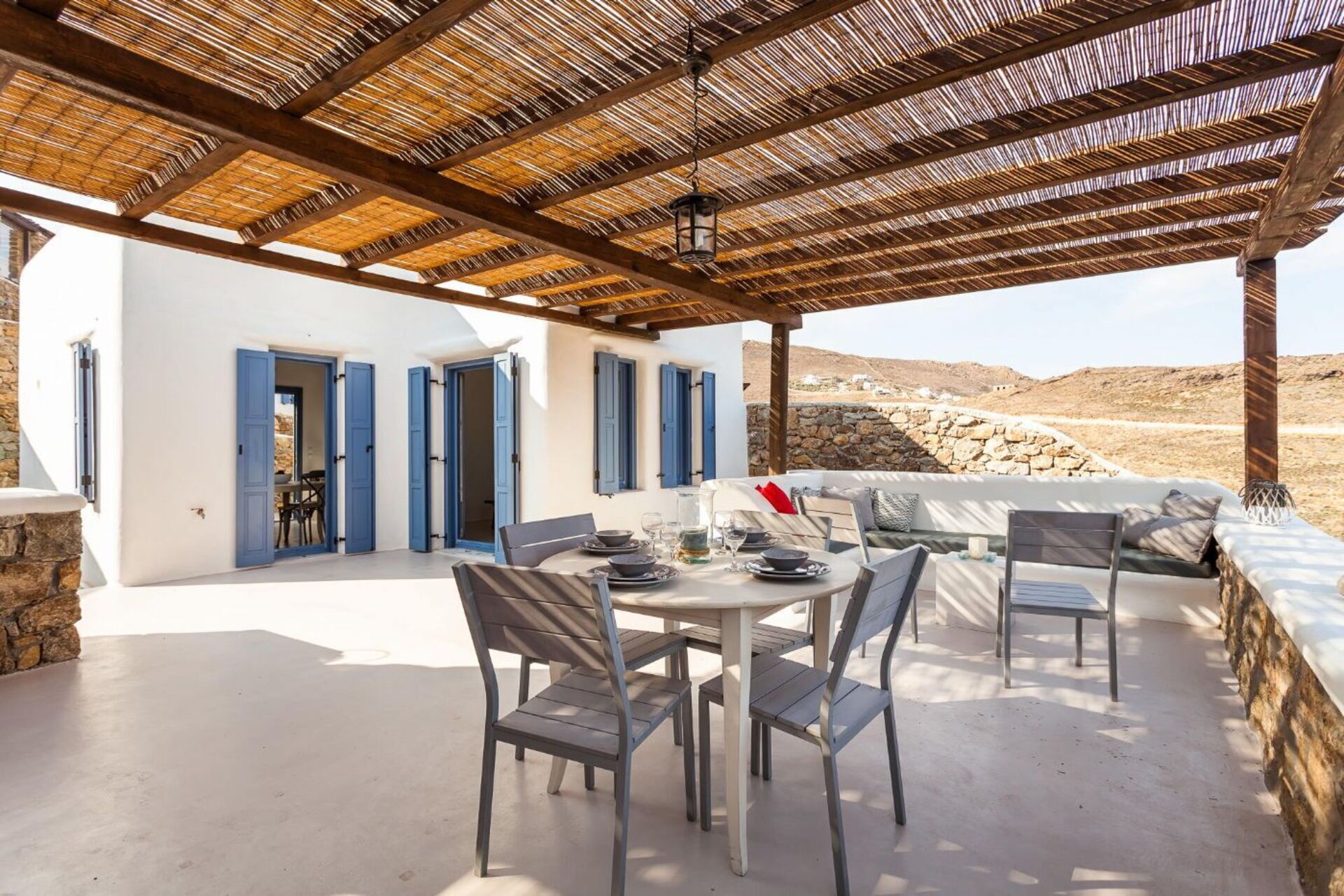Un espacio al aire libre techado con una mesa dispuesta para comer, una pared de piedra y vistas del paisaje.