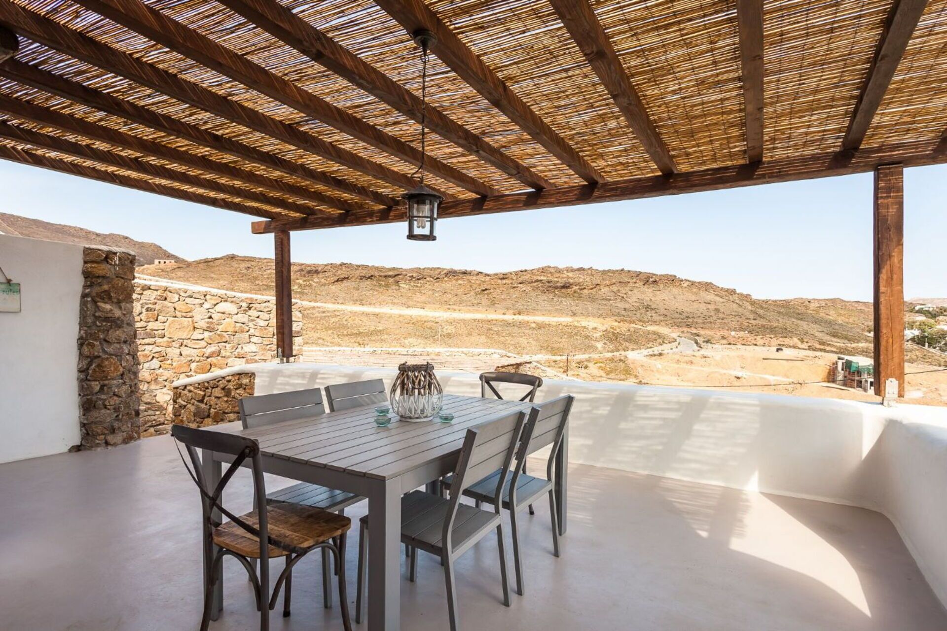 Un patio al aire libre con una mesa y sillas, un muro de piedra y vistas a un paisaje montañoso.