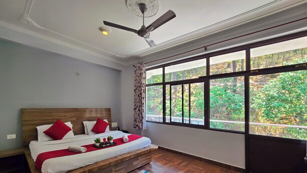 A bedroom with a large window, a ceiling fan, and a wooden bed. - Hotel City Gold - Hotel in Dharamshala (Dharamshala)