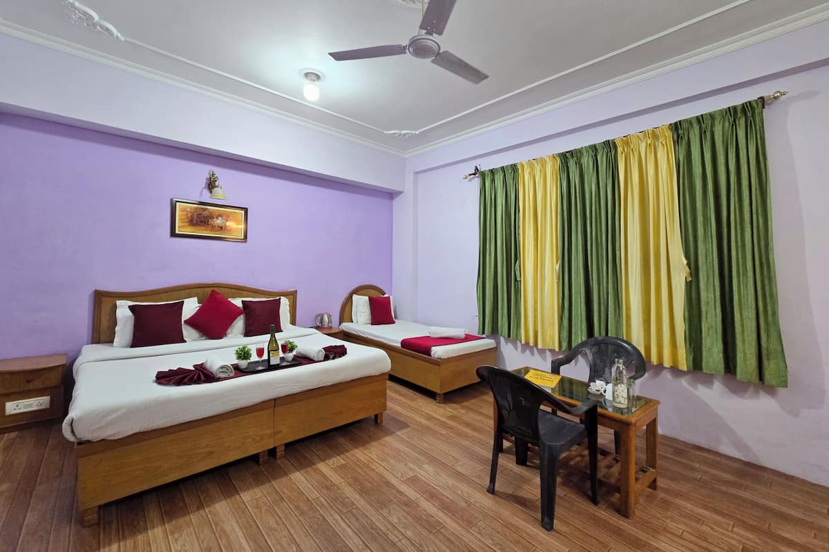 A hotel room with two beds, a ceiling fan, a desk with a chair, and a window with green and yellow curtains.