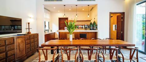 A spacious dining area with a long wooden table, multiple chairs, and a central potted plant.